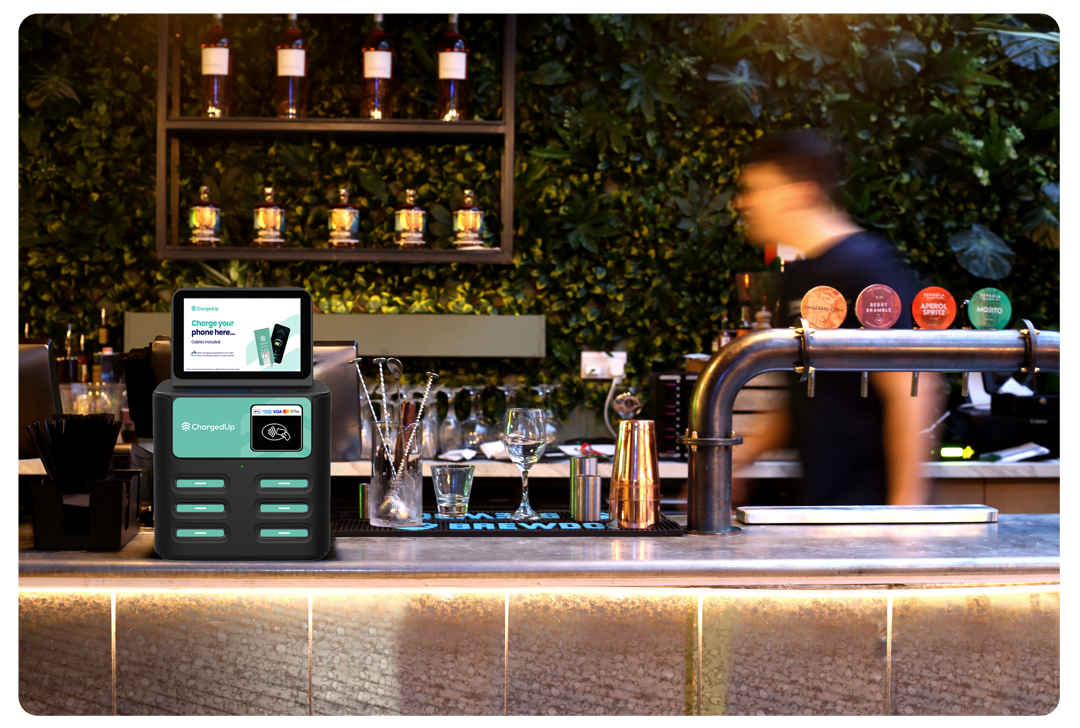 ChargedUp station on a bar counter providing power bank rentals for mobile device charging at a hospitality venue