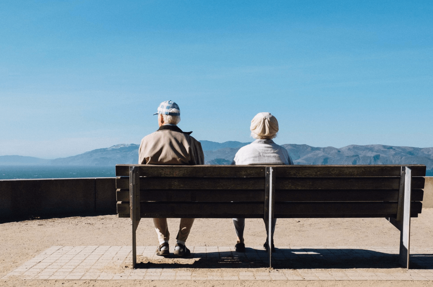 Älteres Ehepaar sitzt auf einer Bank und schaut auf das Meer.