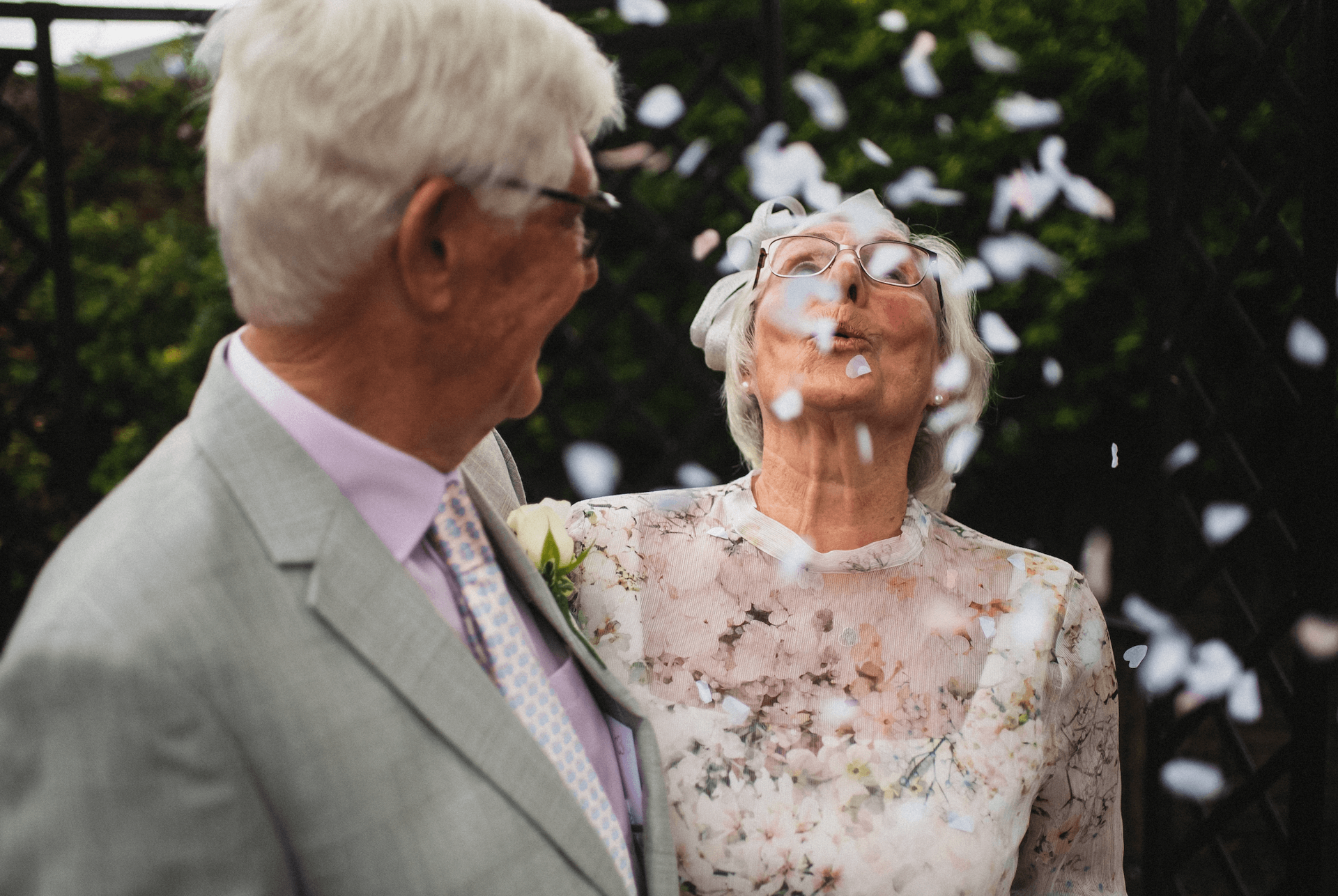Altes Ehepaar umarmt sich und pustet Blumenblätter in die Luft.