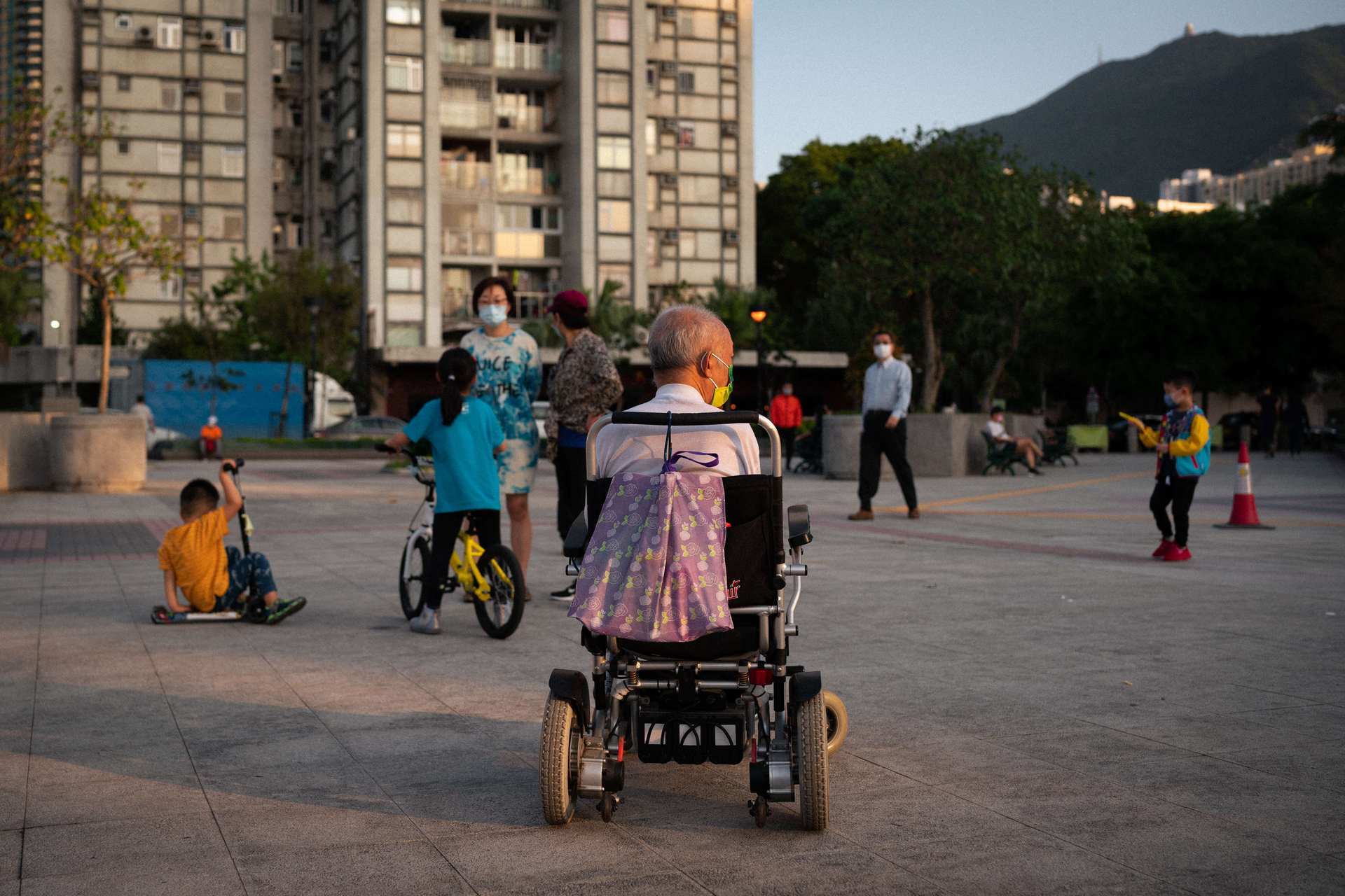 Alter Mann im Rollstuhl beobachtet Kinder auf einem Platz, die spielen.