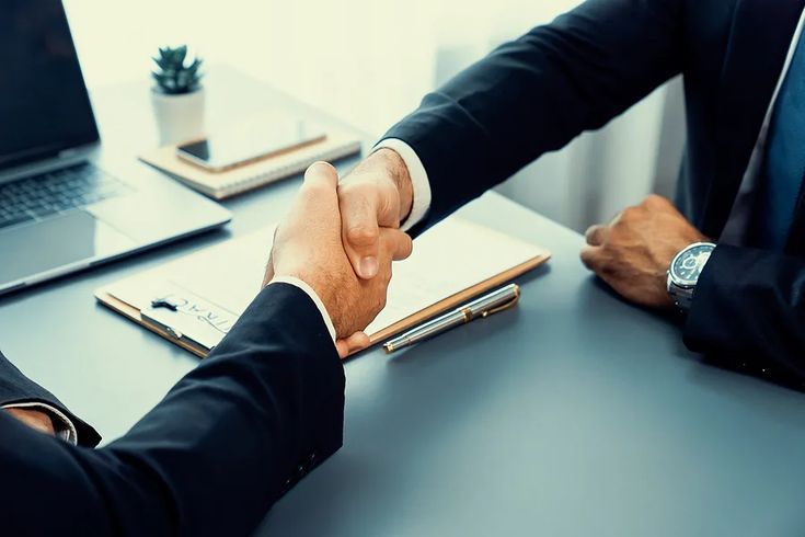 Accord juridique et négociation d’affaires – Deux avocats en costume concluent un partenariat, représentant l’expertise en droit des affaires, fusions & acquisitions du cabinet Asmar & Assayag.