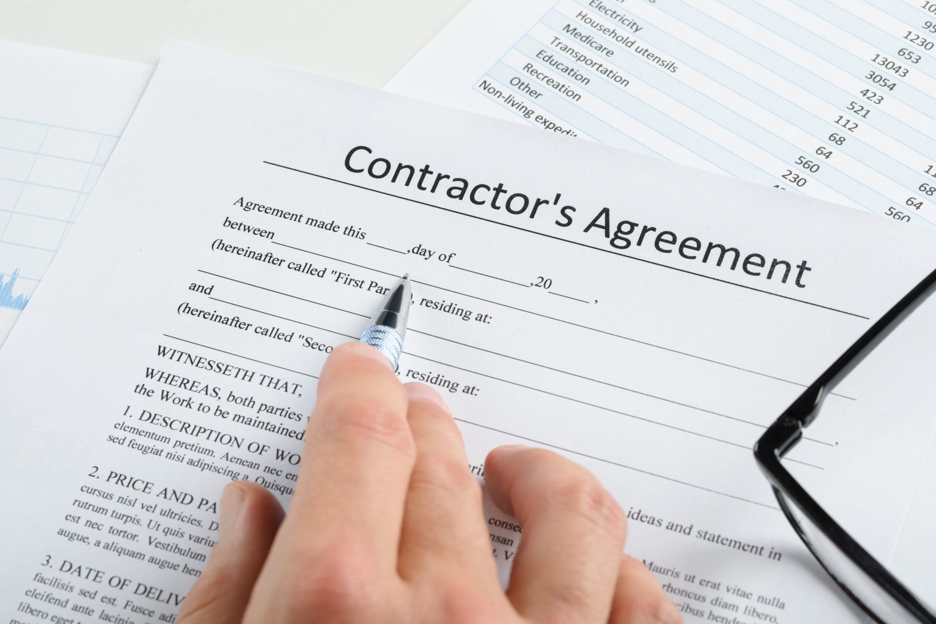 Hand signing a contractor's agreement form with financial documents in the background