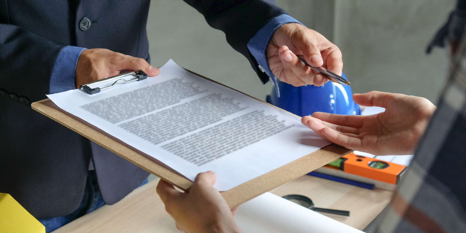 Construction manager handing a contract clipboard and pen to a client for signature